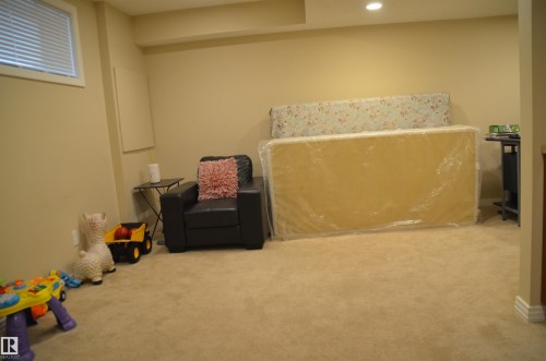 Spacious carpeted room featuring a recessed ceiling light, a high window with blinds, and neutral wall tones - 1412 152, Edmonton, AB - Indoor