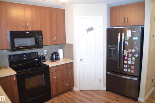 Kitchen with wood-finish cabinetry, light-toned countertops, and a full suite of black and stainless steel appliances - 1412 152, Edmonton, AB 