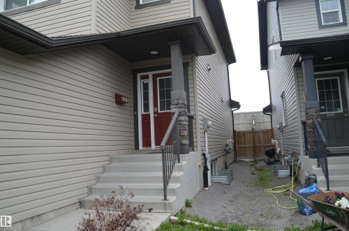 Inviting front entrance featuring a red paneled door, concrete steps, a black metal handrail, and stone accents on porch columns - 1412 152, Edmonton, AB - Outdoor