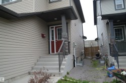 Inviting front entrance featuring a red paneled door, concrete steps, a black metal handrail, and stone accents on porch columns - 