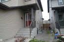 Inviting front entrance featuring a red paneled door, concrete steps, a black metal handrail, and stone accents on porch columns - 1412 152, Edmonton, AB  - Outdoor 