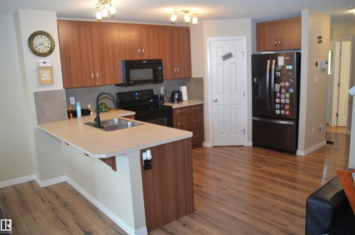 Kitchen featuring wood-finish cabinetry, light-toned countertops, and a full suite of black appliances - 1412 152, Edmonton, AB 