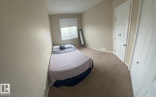 Carpeted room featuring a single window with blinds, beige painted walls, a paneled interior door, and a white bi-fold closet door - 1412 152, Edmonton, AB 