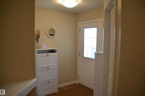 Entryway featuring a white door with a window and grid pattern, wood-finish flooring, and light beige wall paint - 1412 152, Edmonton, AB - Indoor Photo Showing Other Room