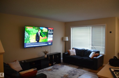 Living area featuring neutral wall tones, a large window with horizontal blinds, and wood-finish flooring - 1412 152, Edmonton, AB - Indoor Photo Showing Living Room