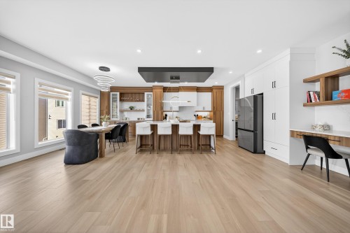 This spacious open-concept area features light hardwood flooring, a modern kitchen with a large island and white countertops, and a dining area with a contemporary chandelier - 6614 39 Avenue, Beaumont, AB - Indoor