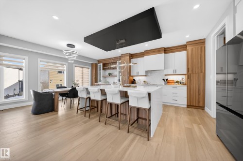This expansive kitchen and dining area features light-toned wood flooring, a central island with seating, white countertops, and a modern light fixture - 6614 39 Avenue, Beaumont, AB - Indoor