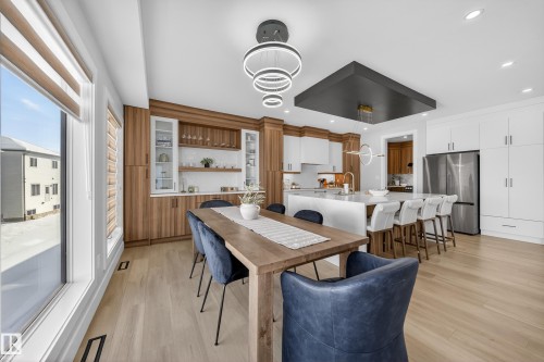 This open-concept living space features light wood flooring, a dining area with a wood table, and a kitchen with white cabinetry and a large island - 6614 39 Avenue, Beaumont, AB - Indoor Photo Showing Dining Room