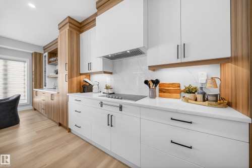 Modern kitchen featuring light wood flooring, white cabinetry with black hardware, and wood-toned accent cabinetry - 6614 39 Avenue, Beaumont, AB - Indoor Photo Showing Kitchen