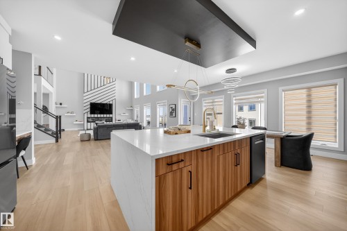 The property features an open-concept living area with light-colored flooring, a kitchen island with a white countertop and wood-toned cabinetry, and a contemporary light fixture - 6614 39 Avenue, Beaumont, AB - Indoor Photo Showing Kitchen