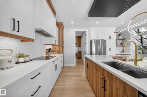 The kitchen features white cabinetry with contrasting wood accents, a stainless steel refrigerator, and a gold-toned faucet - 6614 39 Avenue, Beaumont, AB - Indoor Photo Showing Kitchen With Double Sink With Upgraded Kitchen