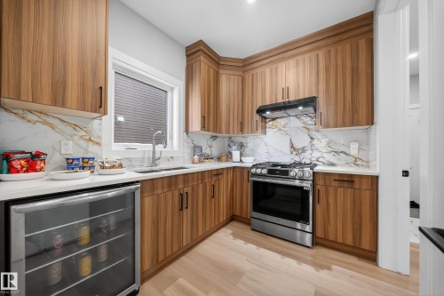 The kitchen features modern wood cabinetry, a white countertop, and a marble-style backsplash - 6614 39 Avenue, Beaumont, AB - Indoor Photo Showing Kitchen