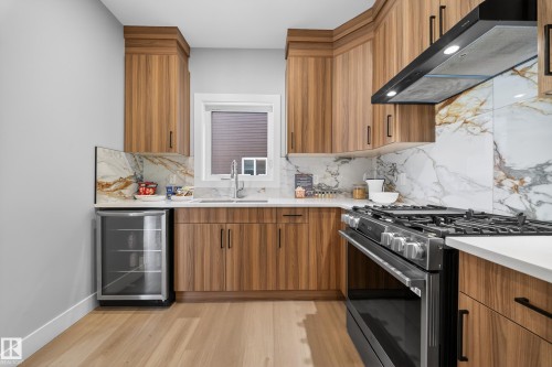The kitchen features modern wood cabinetry, a gas range with a range hood, and a stone backsplash - 6614 39 Avenue, Beaumont, AB - Indoor Photo Showing Kitchen With Upgraded Kitchen