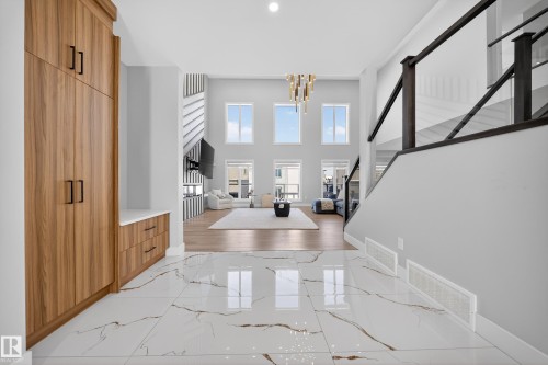 Foyer featuring white marble-style flooring, a built-in wooden storage unit with black hardware, and a modern glass and dark wood railing - 6614 39 Avenue, Beaumont, AB - Indoor Photo Showing Other Room