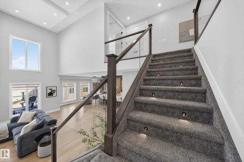 This expansive interior features a grand staircase with carpeted treads and integrated lighting, complemented by a glass and wood railing - 6614 39 Avenue, Beaumont, AB - Indoor Photo Showing Other Room