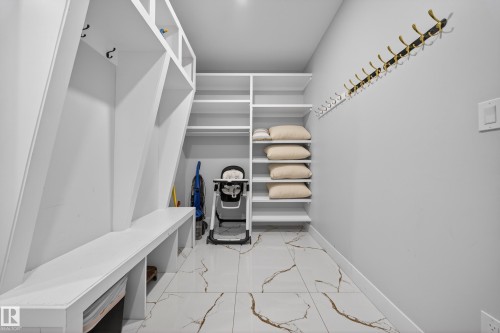 This area features built-in white shelving, a long white bench, and white and brown patterned flooring - 6614 39 Avenue, Beaumont, AB - Indoor
