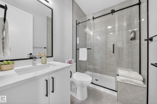 The bathroom features a modern vanity with a marble-patterned countertop, a sleek undermount sink, and a large mirror with a black frame - 6614 39 Avenue, Beaumont, AB - Indoor Photo Showing Bathroom