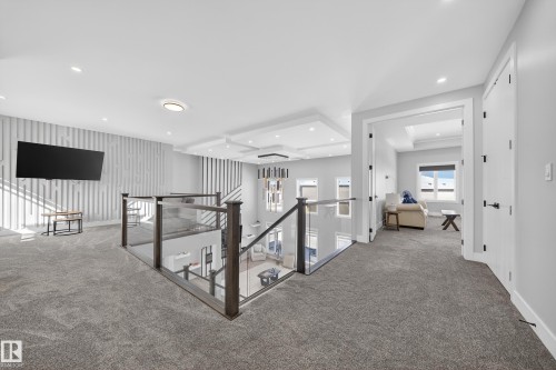 This upper level features a sleek glass railing overlooking the lower floor, recessed lighting, and a decorative accent wall - 6614 39 Avenue, Beaumont, AB - Indoor Photo Showing Other Room