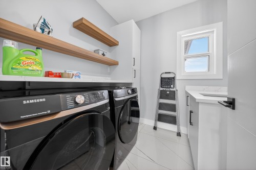 The property includes a dedicated laundry area with a side-by-side washer and dryer, a window, floating shelves, and a countertop with built-in cabinetry - 6614 39 Avenue, Beaumont, AB - Indoor Photo Showing Laundry Room