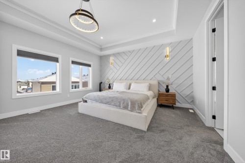 This bedroom features a stylish accent wall with a geometric pattern, a tray ceiling with recessed lighting, and a contemporary chandelier - 6614 39 Avenue, Beaumont, AB - Indoor Photo Showing Bedroom