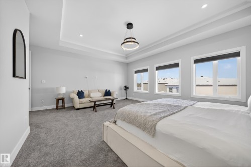 This bedroom features a tray ceiling with recessed lighting, a modern chandelier, and grey carpeting - 6614 39 Avenue, Beaumont, AB - Indoor Photo Showing Bedroom
