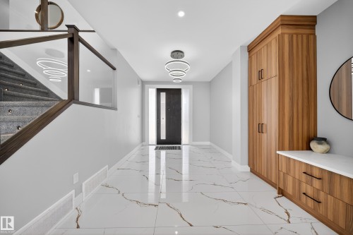The property features a spacious entryway with marbled floors, a modern chandelier, and a built-in wooden storage unit with a white countertop - 6614 39 Avenue, Beaumont, AB - Indoor Photo Showing Other Room