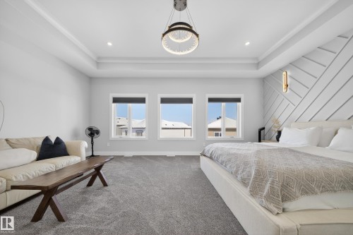 Spacious room featuring three windows providing natural light, a tray ceiling with a contemporary chandelier, and a decorative wall paneling accent - 6614 39 Avenue, Beaumont, AB - Indoor Photo Showing Bedroom