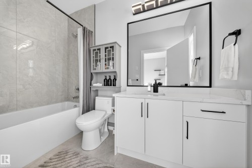 Bathroom featuring a white bathtub, tiled shower surround, and a vanity with a white countertop and dark hardware - 6614 39 Avenue, Beaumont, AB - Indoor Photo Showing Bathroom