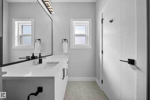 Bathroom featuring a large vanity with a white countertop, an integrated sink, and white cabinetry with black hardware - 6614 39 Avenue, Beaumont, AB - Indoor Photo Showing Other Room