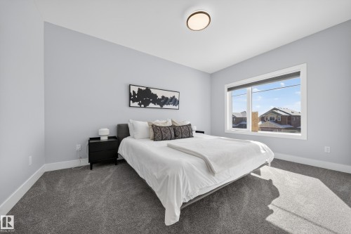 A spacious bedroom featuring light gray walls, a large window providing natural light, and plush gray carpeting - 6614 39 Avenue, Beaumont, AB - Indoor Photo Showing Bedroom