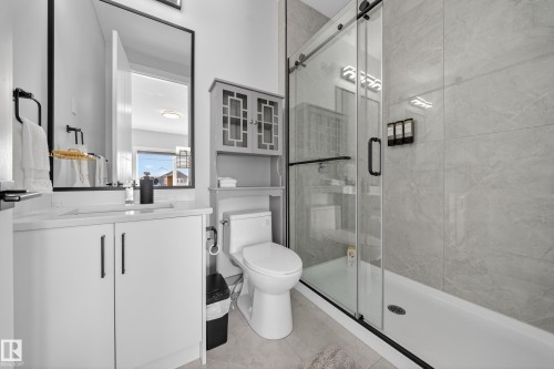 The bathroom features a modern vanity with a white countertop and cabinet, a sleek mirror, and a glass-enclosed shower with light-toned tiled walls - 6614 39 Avenue, Beaumont, AB - Indoor Photo Showing Bathroom