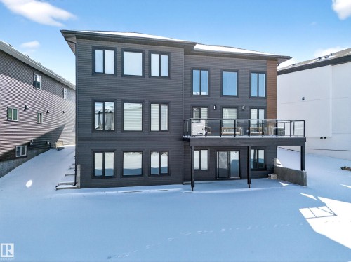 The property features a dark-toned exterior with numerous windows, a deck with a glass railing, and a walk-out patio - 6614 39 Avenue, Beaumont, AB - Outdoor