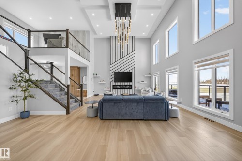This expansive living area features light-toned wood flooring, a striking contemporary chandelier, and a fireplace with a decorative accent wall - 6614 39 Avenue, Beaumont, AB - Indoor