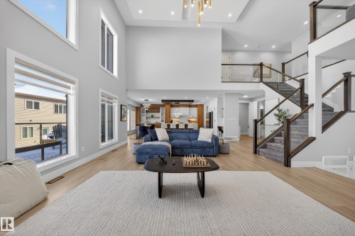 This inviting living area features high ceilings, hardwood floors, and a prominent staircase with glass and wood railings - 6614 39 Avenue, Beaumont, AB - Indoor