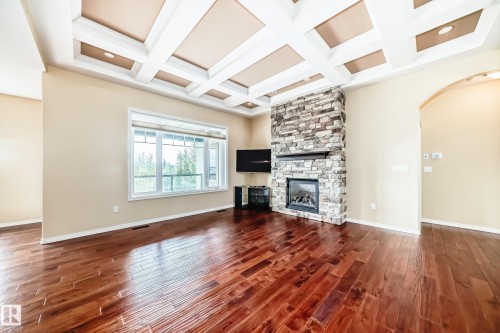Living area featuring a stone-clad fireplace with a dark wood mantel, coffered ceiling with recessed lighting, and rich wood-finish flooring - 527 Callaghan Point(E), Edmonton, AB - Indoor Photo Showing Living Room With Fireplace