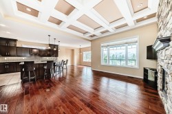 Expansive open-concept living area featuring rich wood-finish flooring, a coffered ceiling, and a prominent stone fireplace - 