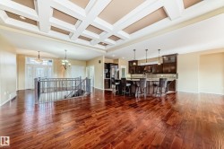 Coffered ceiling with recessed lighting, rich wood-finish flooring, and a kitchen featuring dark wood cabinetry and a large island with pendant lighting - 