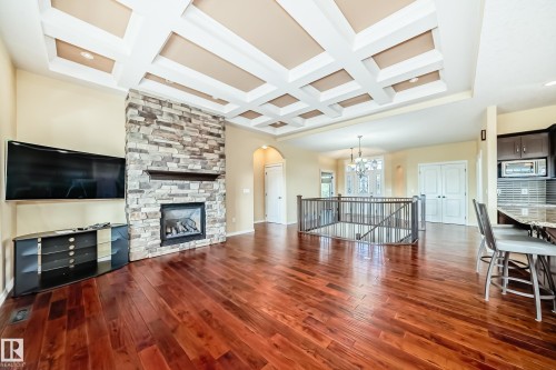 Open-concept interior featuring rich wood-finish flooring, a coffered ceiling with recessed lighting, and a stone-clad fireplace with a wood mantel - 527 Callaghan Point(E), Edmonton, AB - Indoor Photo Showing Living Room With Fireplace