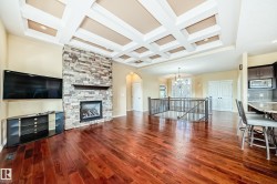 Open-concept interior featuring rich wood-finish flooring, a coffered ceiling with recessed lighting, and a stone-clad fireplace with a wood mantel - 