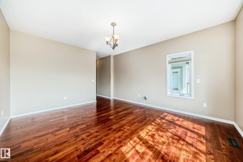 Spacious room featuring rich wood-finish flooring, neutral wall tones, a contemporary chandelier, and a framed interior window - 527 Callaghan Point(E), Edmonton, AB - Indoor Photo Showing Other Room