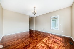 Spacious room featuring rich wood-finish flooring, neutral wall tones, a contemporary chandelier, and a framed interior window - 
