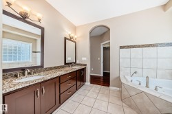 Bathroom featuring a dual vanity with granite countertop, tiled flooring, and a built-in soaking tub with a tiled surround - 