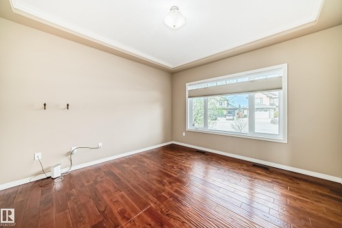 Spacious room featuring rich wood-finish flooring, a large window with roller shades, and a tray ceiling with crown molding - 527 Callaghan Point(E), Edmonton, AB - Indoor Photo Showing Other Room
