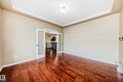 Spacious room featuring rich wood-finish flooring, a tray ceiling with crown molding, and double French doors with frosted glass panels - 527 Callaghan Point(E), Edmonton, AB - Indoor Photo Showing Other Room
