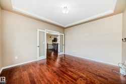 Spacious room featuring rich wood-finish flooring, a tray ceiling with crown molding, and double French doors with frosted glass panels - 