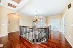 Upper-level landing featuring rich wood-finish flooring, an ornate staircase railing, a decorative chandelier, recessed lighting, and a tray ceiling detail - 
