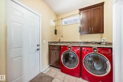 Integrated laundry area featuring wood-finish cabinetry, granite-style countertops, mosaic tile backsplash, and a utility sink - 