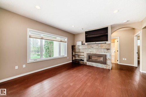 Spacious interior featuring rich wood-finish flooring, a broad window with horizontal blinds, and recessed ceiling lighting - 527 Callaghan Point(E), Edmonton, AB - Indoor Photo Showing Living Room With Fireplace