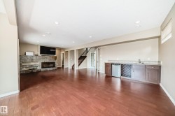 Spacious interior featuring wood-finish flooring, a stone-clad fireplace, and a built-in wet bar with cabinetry and a beverage refrigerator - 