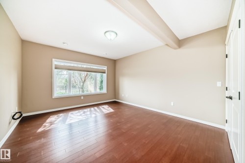 Spacious room featuring rich wood-finish flooring, a large window with roller shades, and a ceiling beam - 527 Callaghan Point(E), Edmonton, AB - Indoor Photo Showing Other Room